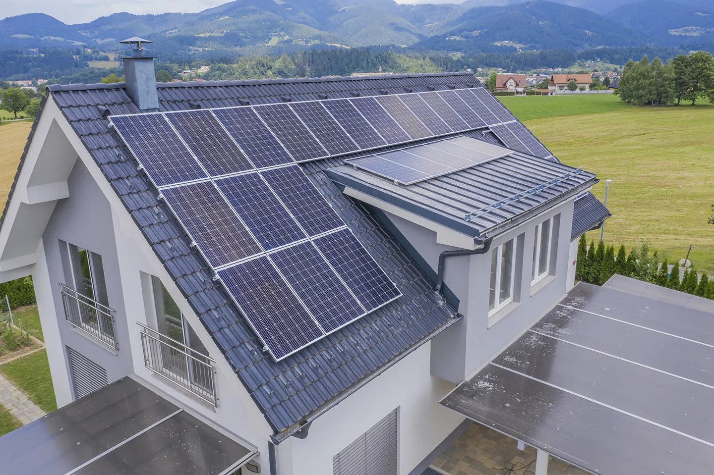 Luftaufnahme eines Einfamilienhauses, dessen Satteldach voll mit Solarmodulen belegt ist, dahinter eine Hügellandschaft
